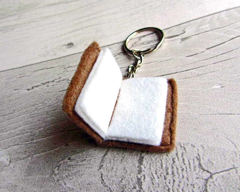 May include: A brown felt book keychain with a white interior and a silver key ring.