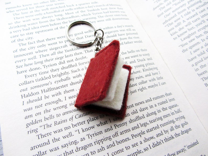 May include: A red and white felt book charm with a silver key chain. The charm is a miniature book with a red cover and white pages. The keychain is attached to a silver ring.