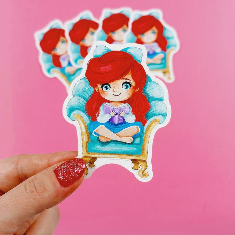 May include: A die-cut sticker featuring a cartoon character with vibrant red hair and a light blue bow, sitting cross-legged in a gold-trimmed teal armchair while reading a purple book. The character has large blue eyes and a white shirt.