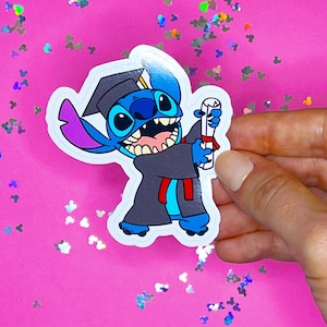 May include: A blue Stitch character wearing a graduation cap and gown, holding a diploma. The character is smiling and has a red sash.