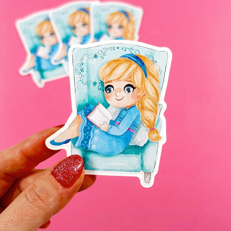 Pu&ograve; includere: Un adesivo con un'illustrazione di cartone animato di una ragazza con lunghi capelli biondi che legge un libro mentre &egrave; seduta su una poltrona blu. La ragazza indossa un vestito blu con un motivo a fiocco di neve bianco e una fascia per capelli blu. Lo sfondo &egrave; un acquerello blu chiaro.