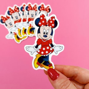 May include: A red and white polka dot Minnie Mouse sticker with a white outline. The sticker features Minnie Mouse in a red dress with white polka dots and a red bow with white polka dots.