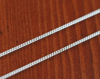 Könnte beinhalten: Eine silberne Kettenkette im Curb-Link-Stil. Die Kette liegt auf einer Holzoberfläche.
