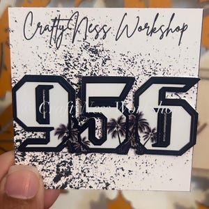 May include: Black and white number 956 with palm tree graphics. The numbers are outlined in black and have a white background. The numbers are on a white background with black splatter paint.