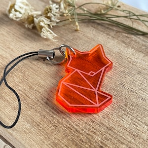 Könnte beinhalten: Orangener Acryl-Schlüsselanhänger mit geometrischem Fuchs-Design. Der Schlüsselanhänger hat eine schwarze Schnur.