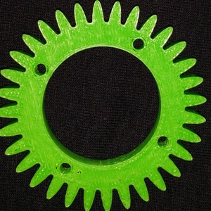Puede incluir: Un engranaje de plástico verde brillante con un gran agujero central y cuatro agujeros más pequeños alrededor del borde exterior.