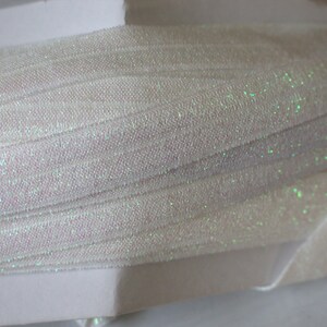 May include: White iridescent tulle fabric with a subtle shimmer. The fabric is folded and layered, showing the texture and sparkle.