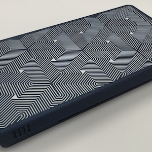 May include: A dark blue rectangular device with a white geometric pattern on the top. The device has a small black power button on the side.