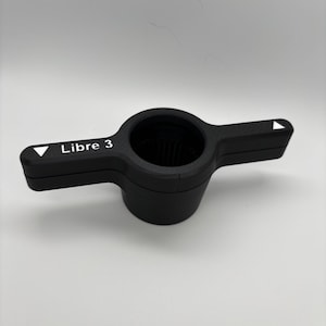 May include: Black plastic Libre 3 sensor with a white label and two white arrows on the sides.