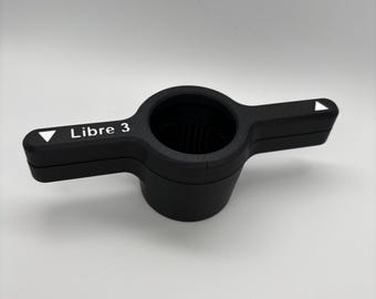 May include: Black plastic Libre 3 sensor with a white label and two white arrows on the sides.