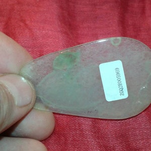 May include: A translucent, teardrop-shaped pendant with a pale green hue and a small, attached label. The pendant has a subtle, cloudy appearance and a small hole at the top. The label displays the text "ZCQ2E005969".