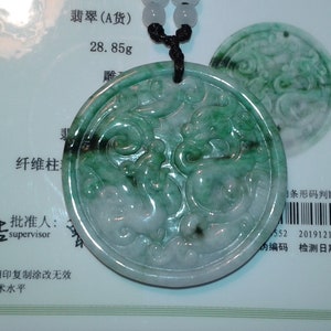 May include: A circular jade pendant with a dragon carving, in shades of green and white, suspended on a black cord. The pendant weighs 28.85 grams. The design is intricate and detailed.