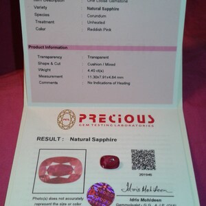 May include: A gemmological report detailing a natural, reddish-pink sapphire. The report shows the gemstone's weight (4.40 ct), measurements (11.30x7.91x4.84 mm), and shape (cushion/mixed). The report is from Precious Gem Testing Laboratories.