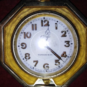 May include: An antique octagonal clock with a white face and gold-colored trim. The clock face features black numerals, hands, and the text "TIFFANY & CO.". The clock is marked "8 Days" and "PAT MAY 5TH. 1903. FEB. 4 1908."