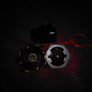May include: A black and yellow spinning top toy with a silver and black base, a black launcher, and a red pull string. The toy is designed for competitive play and features a unique design.