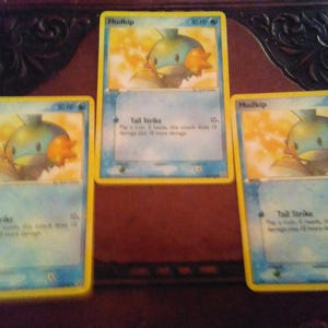 May include: Three Pokemon trading cards featuring the Mudkip character. Each card has a yellow border, a blue background, and a picture of Mudkip. The text "Mudkip" and "Tail Strike" are visible on the cards.