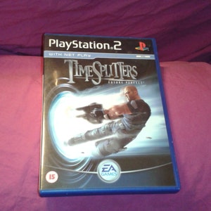 Puede incluir: Caja de videojuego de PlayStation 2 para Timesplitters: Future Perfect. La portada muestra a un hombre con un arma, saliendo de un portal brillante. La caja es azul con el logo de PlayStation 2 en la parte superior.