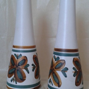 May include: Two white ceramic vases with a flared base and a narrow top. The vases feature a floral design in brown and teal, with brown and teal bands. The vases are approximately 30 cm tall.