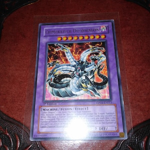 May include: A Yu-Gi-Oh! trading card featuring "Chimeratech Overdragon." The card has a purple background with a dragon illustration and text. The card is in a protective sleeve.