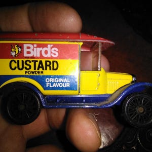 May include: A vintage toy delivery truck with a red roof, yellow body, and blue accents. The truck features the "Bird's Custard Powder" logo and "Original Flavour" text. The wheels are black.