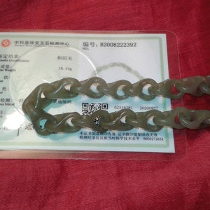 May include: A jade bracelet with a chain link design, displayed on a red surface. The bracelet is a muted green color. A certificate with Chinese text is visible in the background, with the total weight listed as 18.14g.