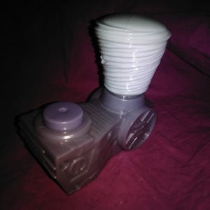 May include: A gray and purple toy with a white, spiraled top. The toy has a rectangular base with a circular purple button and a cylindrical body with a wheel-like design.