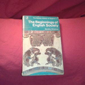 May include: A vintage book titled "The Beginnings of English Society" by Dorothy Whitelock. The book has a teal and white cover with decorative illustrations. The book is part of "The Pelican History of England" series.