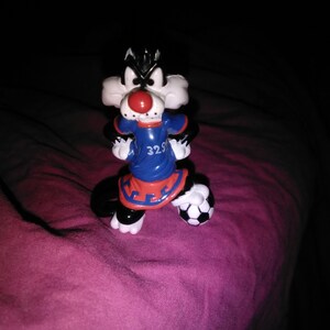 Op de afbeelding: Een Sylvester de Kat-beeldje in een voetbaltenue. Het beeldje is zwart en wit met een rode neus en een blauw en rood tenue. De voetbal is zwart en wit.