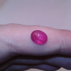 Op de afbeelding: Een ovale, gepolijste, roze edelsteen. De doorschijnende steen wordt in een hand gehouden en toont zijn interne lichtbreking. De kleur van de edelsteen varieert van diep magenta tot een lichter roze.