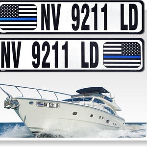 May include: Two black and white boat registration stickers with a thin blue line American flag. The stickers read "NV 9211 LD". The stickers are displayed on a white background. A white boat is in the background.