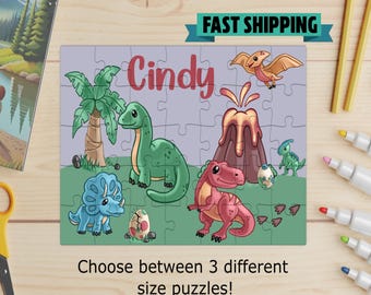 May include: A personalized dinosaur-themed jigsaw puzzle with the name "Cindy" in red. The puzzle features cartoon dinosaurs, a volcano, and a palm tree. The text "FAST SHIPPING" is displayed above the puzzle, and "Choose between 3 different size puzzles!" is displayed below.