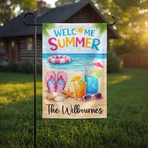 May include: A rectangular garden flag featuring the text WELCOME SUMMER and The Wilbournes. The design shows a beach scene with a pink and white striped inner tube, pink flip-flops, seashells, a starfish, two drinks with fruit, and pink sunglasses.