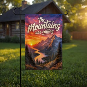 May include: A rectangular garden flag hanging on a black metal stand. The flag features a vibrant sunset over a mountain range and a winding river, with dark pine trees in the foreground. The text "The Mountains are calling" is printed in white.