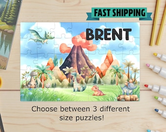May include: A personalized jigsaw puzzle featuring the name "BRENT" in black block letters. The puzzle depicts a colorful prehistoric landscape with dinosaurs, a volcano, and palm trees. The text "Choose between 3 different size puzzles!" is also visible.