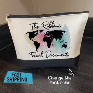 May include: A canvas travel pouch with a black base and a white upper section. The pouch features a world map design with watercolor accents in pink, blue, and green. Text on the pouch reads "The Robbin's Travel Documents". A silver zipper is visible.