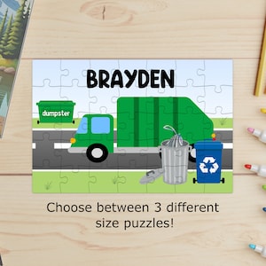 May include: A personalized puzzle featuring a green garbage truck, a dumpster, and recycling bins. The name "BRAYDEN" is displayed in large black letters. The puzzle includes the text "Choose between 3 different size puzzles!"