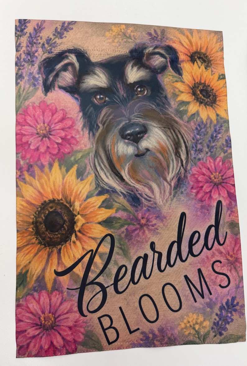 May include: A rectangular garden flag featuring a portrait of a black and grey Schnauzer dog surrounded by yellow sunflowers, pink zinnias, and purple lavender. The text "Bearded BLOOMS" is printed in black script and block lettering at the bottom.