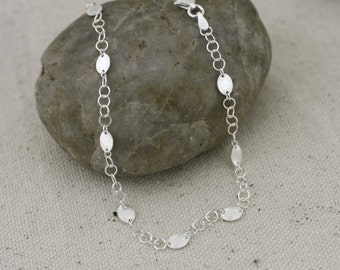 Puede incluir: Un brazalete de cadena de plata con eslabones de forma ovalada. Los eslabones tienen una superficie texturizada y están espaciados a lo largo de la cadena.