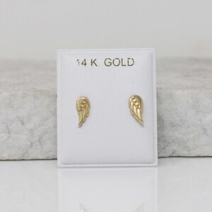 Puede incluir: Un par de pendientes de alas de &aacute;ngel de oro en una tarjeta blanca con el texto "14K GOLD".