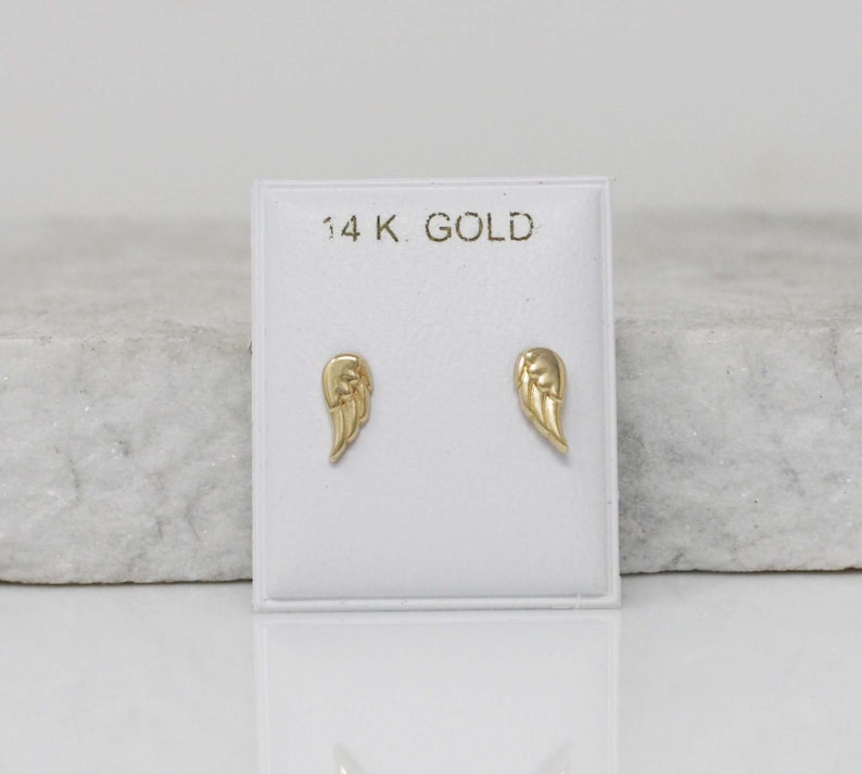 Puede incluir: Un par de pendientes de alas de &aacute;ngel de oro en una tarjeta blanca con el texto "14K GOLD".