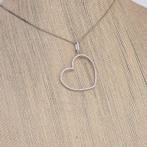 Op de afbeelding: Een zilveren ketting met een hartvormige hanger die is bezet met kleine diamanten.