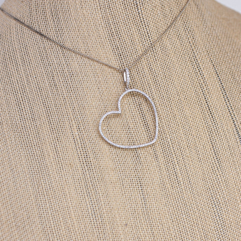 Op de afbeelding: Een zilveren ketting met een hartvormige hanger die is bezet met kleine diamanten.