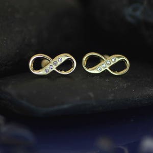 Op de afbeelding: Een paar gouden oorringen in de vorm van een oneindigheidssymbool met heldere zirkonia-stenen.