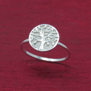 May include: A silver ring with a tree of life design. The ring is on a red background.