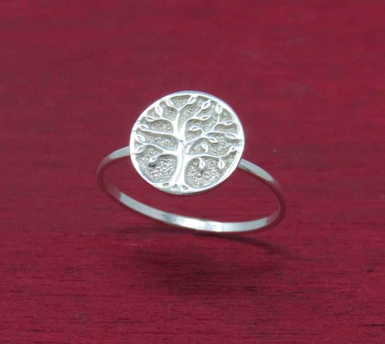 May include: A silver ring with a tree of life design. The ring is on a red background.