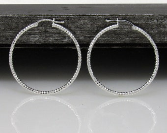 May include: A pair of silver hoop earrings with a textured finish. The earrings are circular and have a hinged closure.