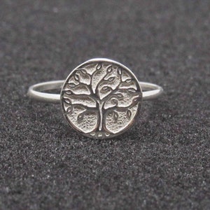 May include: A silver ring with a tree of life design. The ring is round and has a detailed design of a tree with branches and leaves.