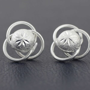 May include: A pair of silver earrings with a textured, circular design. Each earring features a central circle with a star-shaped pattern.