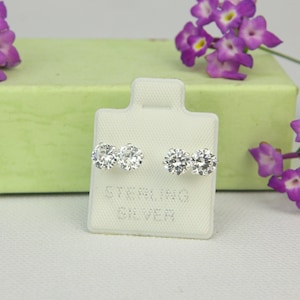 May include: A pair of sterling silver earrings with three round cubic zirconia stones each. The earrings are displayed on a white card with the words "Sterling Silver" printed on it.
