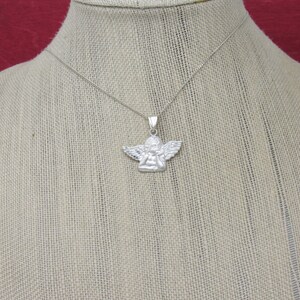 May include: A silver chain necklace with a small silver angel pendant. The angel is depicted with wings and a prayerful pose.